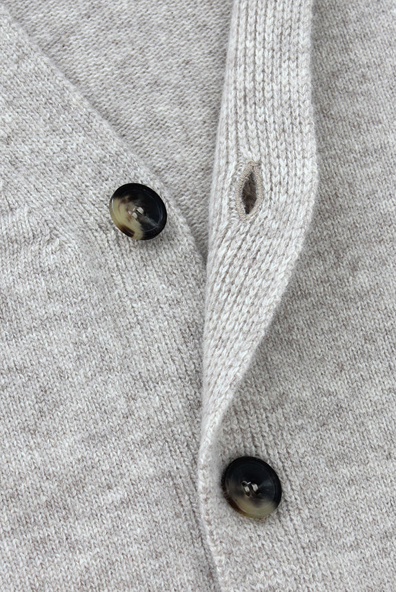 Close-up of a gray knitted cardigan with black buttons on a matching fabric background
